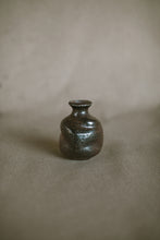 Load image into Gallery viewer, A small brown and black bud vase on a beige fabric background. The piece is made from Iron rich Australian stoneware clay wood ash covering one side.