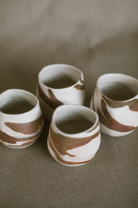 Four white and brown tumblers on a beige fabric background. These pieces are made from white Australian stoneware clay with brown and white marbled clay inlaid during the wheel throwing process.