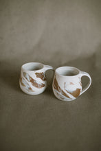 Load image into Gallery viewer, Two white and brown mugs on a beige fabric background. The pieces are made from white Australian stoneware clay with brown and white marbled clay inlaid during the throwing process.