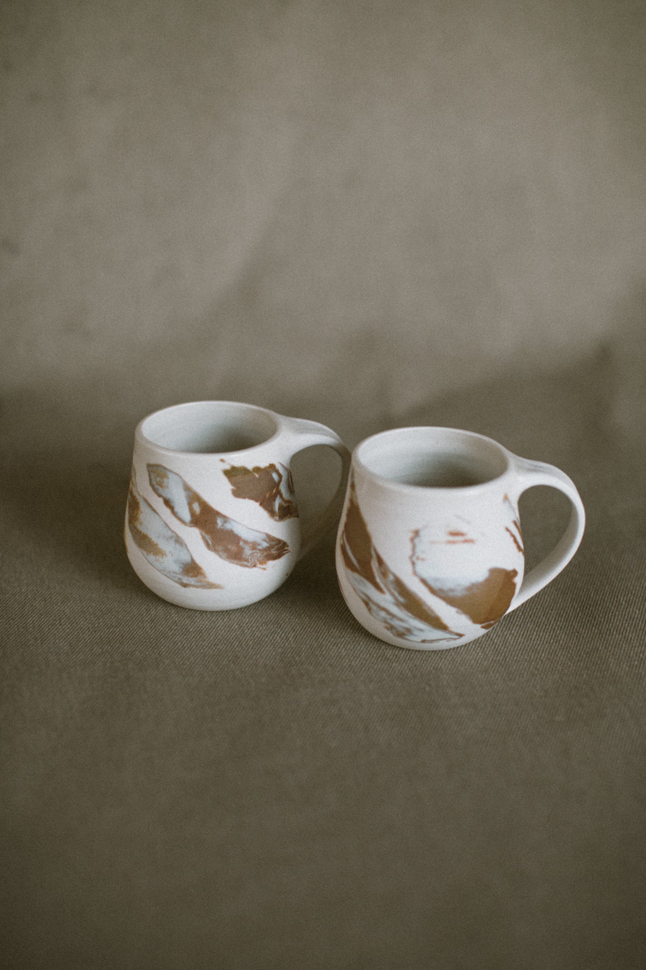 Two white and brown mugs on a beige fabric background. The pieces are made from white Australian stoneware clay with brown and white marbled clay inlaid during the throwing process.