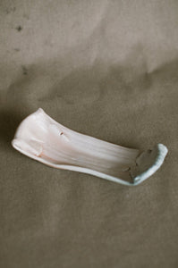A wood fired platter on a beige fabric background. This wheel thrown stretched platter is made from white Australian stoneware clay with pale green ash on one end and light peach flashing on the other.