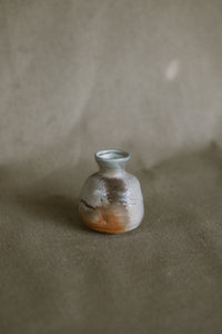  small white and orange bud vase on a beige fabric background. The piece is made from white Australian stoneware clay flame markings on one side. 