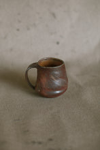 Load image into Gallery viewer, A dark brown mug on a beige fabric background. This piece is made from iron rich Australian stoneware clay that has turned an almost metallic brown in the wood kiln. Inside is a light orange Shino glaze