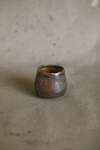 Load image into Gallery viewer, A small dark brown wood fired cup on a beige fabric background. This wheel thrown and altered Japanese inspired yunomi is made from dark Iron rich Australian stoneware clay that has a Shino glaze inside.