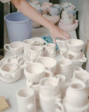 Load image into Gallery viewer, A table full of white bisque pottery waiting to be glazed in different colours