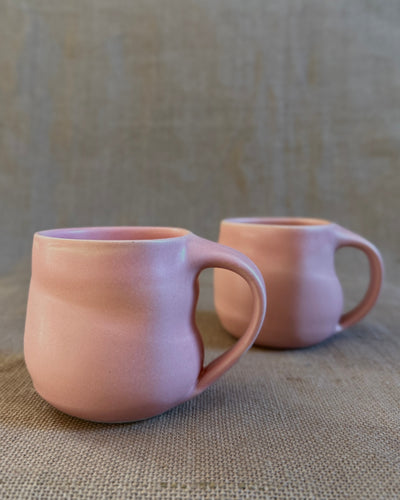 Two pink ceramic mugs on a textured beige surface