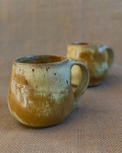 Load image into Gallery viewer, Two ceramic mugs with a brown and gold glaze on a textured brown surface.