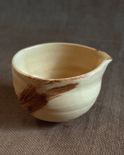 Yellow ceramic matcha bowl with brown accents on a textured brown surface
