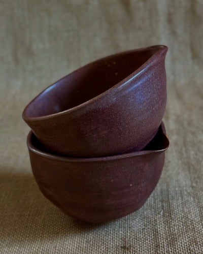 Two dark red ceramic matcha bowls stacked on a textured beige background