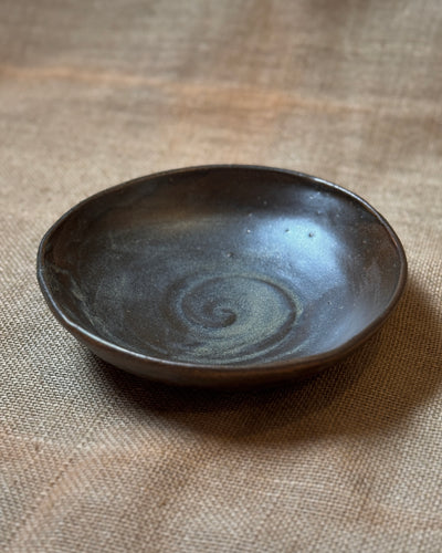 Ceramic pasta bowl with a metallic black glaze sitting on a textured beige surface