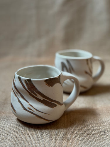 Two ceramic mugs with brown abstract patterns on a textured surface