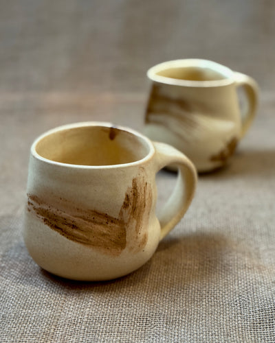 Two yellow glazed ceramic mugs with brown accents on a textured surface
