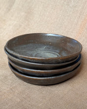 Load image into Gallery viewer, A stack of shallow pasta bowls made from stoneware glazed in a dark brown and black on a beige fabric background